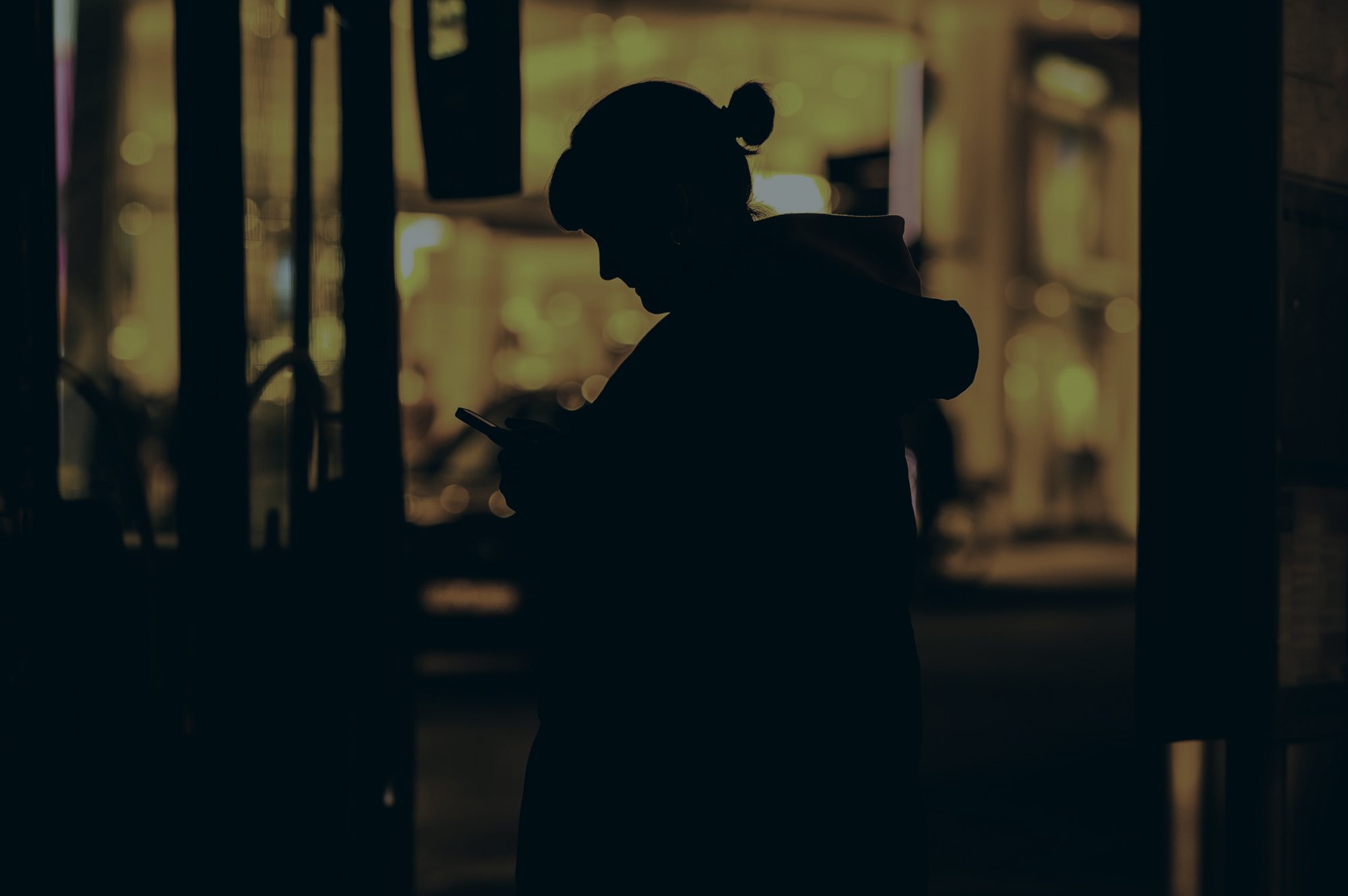 A person silhouetted on a street at night, reading a phone